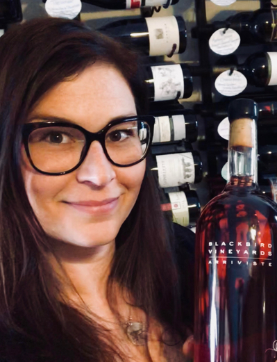 Person infront of wine rack holding up Arriviste Bottle for the camera